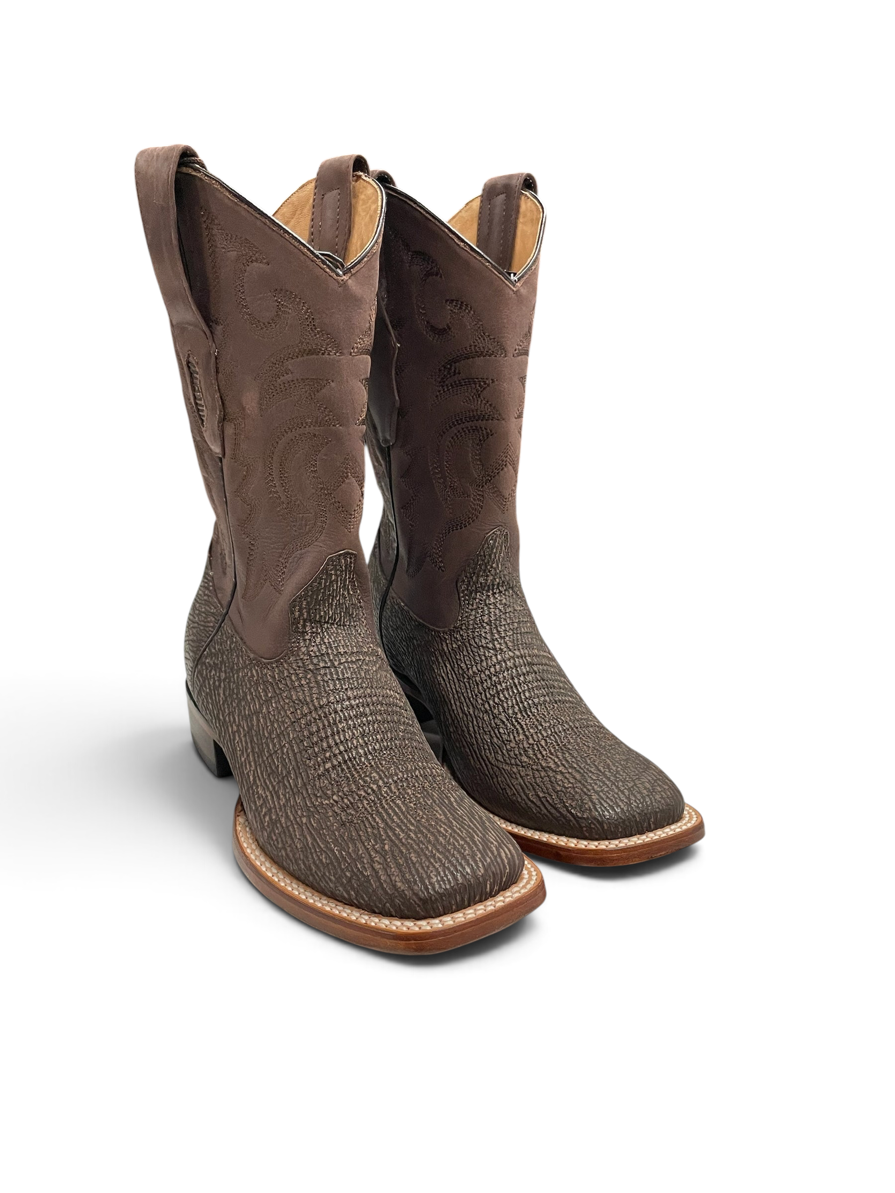 Botas vaqueras Botas El Pistolero PYP de piel de tiburón marrón con punta cuadrada y caño bordado sobre mesa de mármol