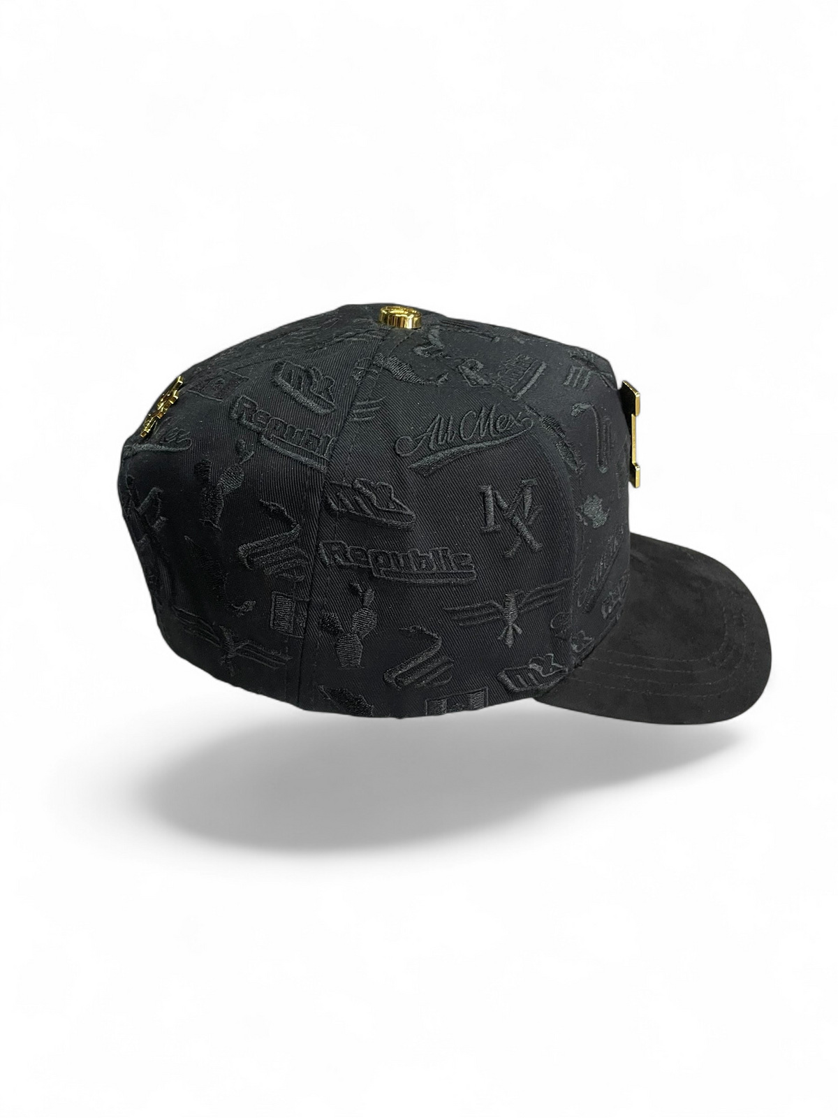 Gorra Botas El Pistolero PYP negra con textura grabada, emblema metálico dorado y detalles de lujo en estilo urbano.